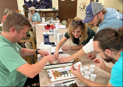 Four people leaning over a table take part in an activity involving rubber bands.